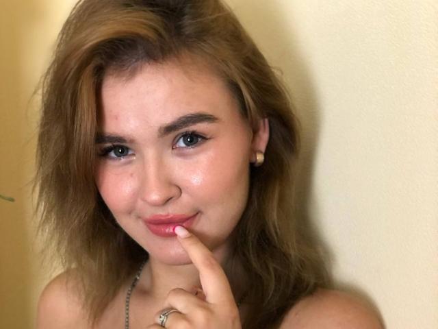 SofiVernara ha i capelli biondo cenere, gli occhi azzurri e un sorriso carino, con un dito che tocca le sue labbra rosa lucide. Indossa un orecchino di perle e una collana d'argento..