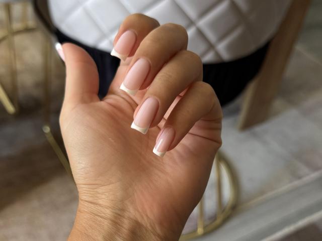 EricaLust's hand with pink and white French tip nails, showing off her neatly manicured, soft pink, glossy nails against a blurred background.