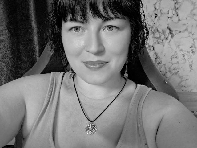 Black-and-white selfie of SweetsKiss with short dark hair, bangs, wearing a tank top, necklace with a star pendant, and earrings, smiling softly at the camera.