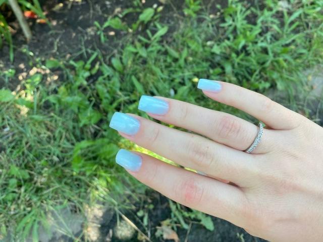 La mano de Kripkoa, con uñas de color azul claro y con forma cuadrada, y un anillo de plata en su dedo, descansando sobre la hierba verde..