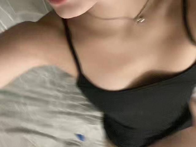 Os pequenos seios de Kripkoa, cobertos por uma blusa preta com alças finas, com um colar fino e parte do rosto visível, fotografados de um ângulo superior..