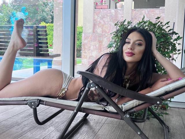 PamelaMoon with long black hair, lying on a folding chair, wearing a leopard-print bikini, showing her ass, legs up, in a sunlit room, near a pool.