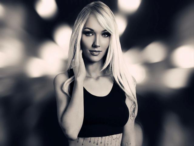 Ginacolada-hot with long blonde hair, black sports bra, and tattooed midriff, hand on face, looking seductively at camera, bokeh effect in background, monochrome, soft light.