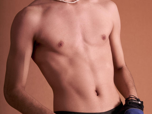 NovaWheeler's bare, slim, toned torso with small, flat nipples and a slight belly button, wearing a pearl necklace and black pants with a blue pocket.