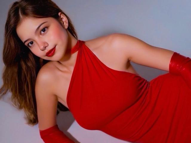 EmilyVelours with red dress, red gloves, and red lipstick, showing her tits and smiling at the camera, has long brown hair, and a cute, sexy look.