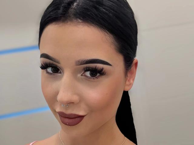 TaliaClassy-hot has dark hair, thick eyebrows, long eyelashes, a nose ring, and brown lipstick. She's looking at the camera with a slight smile.