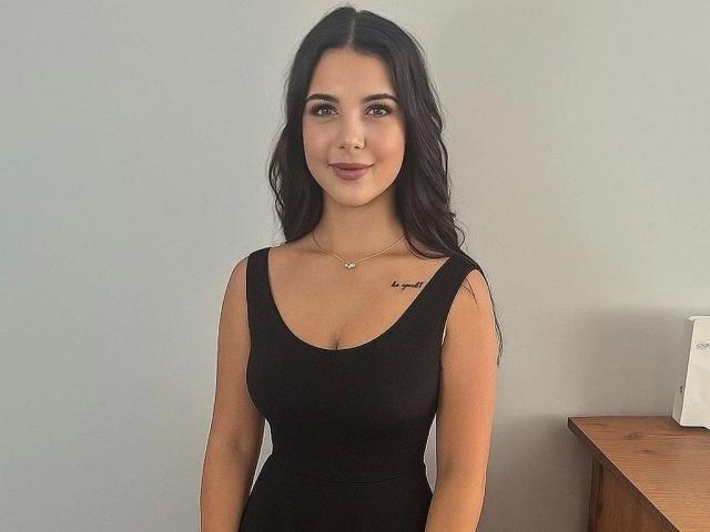 TaliaClassy-hot has long black hair, brown eyes, and a cute smile. She's wearing a black dress, showing her boobs, and has a small tattoo on her right shoulder.