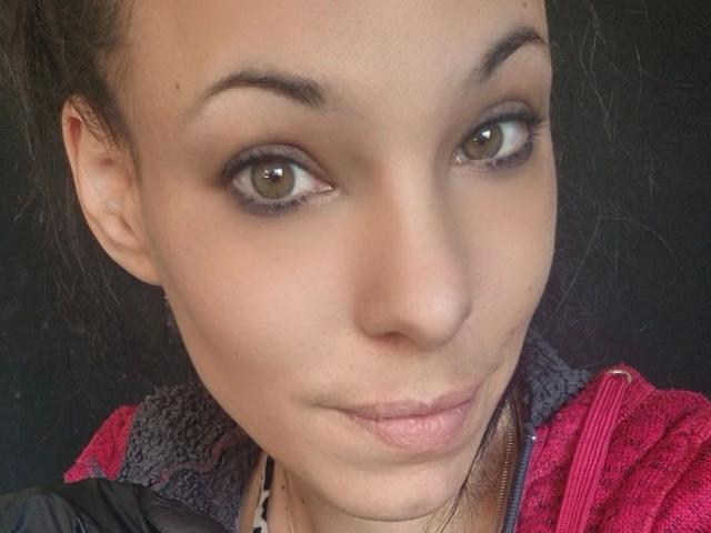 SexyAnnabell38-hot has light brown eyes, dark eyebrows, and a slight smile with puffed-up lips. She's wearing a red and black jacket with a furry collar.