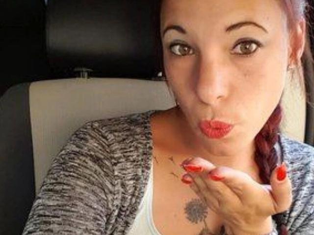 SexyAnnabell38-hot is pouting with red lipstick, wearing a grey cardigan, and showing off her red nails with a tattoo on her chest. She has a red braid.