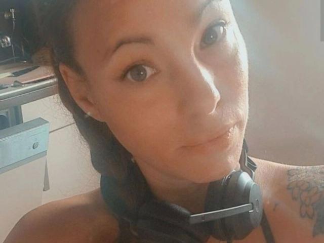 SexyAnnabell38-hot with headphones on, brown eyes, slight smile, light skin, small tattoo on right shoulder, brown hair, and a soft, natural light on her face.