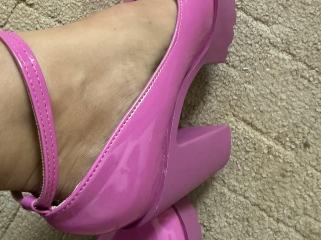 MargoRoiss' rosaroter, glänzender High-Heel-Schuh befindet sich an ihrem Fuß, wobei ihr Knöchel und ein wenig ihrer Haut zu sehen sind, und darunter liegt ein strukturierter Teppich..