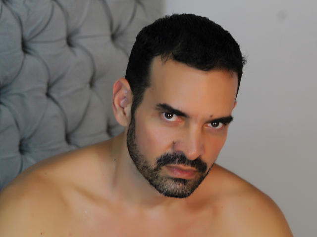 XRawForU has a serious, slightly annoyed expression, dark short hair, a trimmed beard, and a shirtless, muscular upper body with a light skin tone.