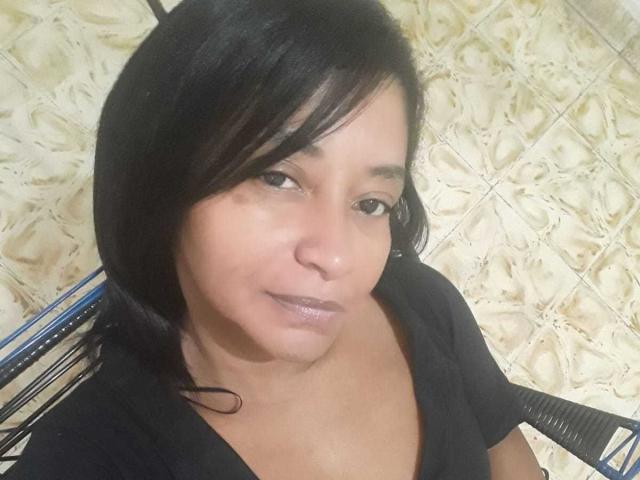 ShareLonnie has short black hair, brown eyes, and a slight smile. She's wearing a black shirt, showing a bit of cleavage. Her face is slightly shiny.