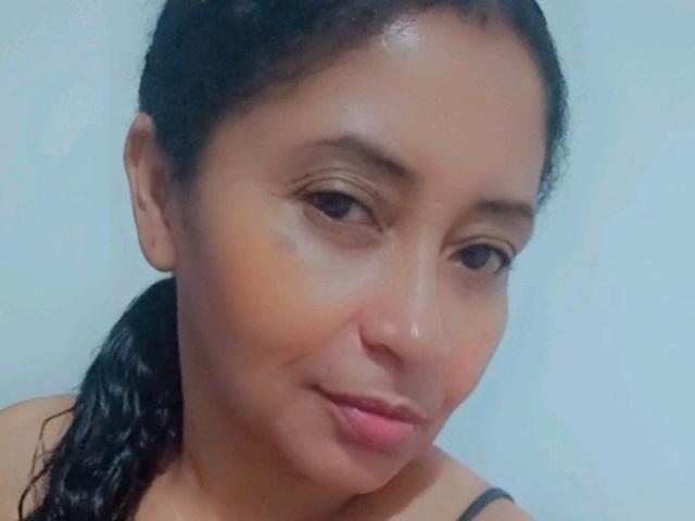 ShareLonnie has light brown skin, dark wet hair in a ponytail, subtle eyeliner, pink lipstick, and a slight smile. She's wearing a black strap top.