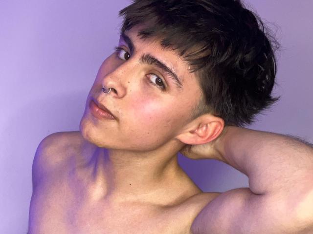 PepperTwink has short, messy black hair, a nose ring, and is shirtless with a lean, muscular upper body. They're looking to the side with a slight, confident smirk.