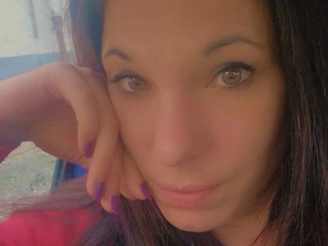 SexyAnnabell38-hot with brown eyes, purple nails, and dark brown hair, leaning on her cheek, showing a subtle smile, soft pink lips, and a slight tan.