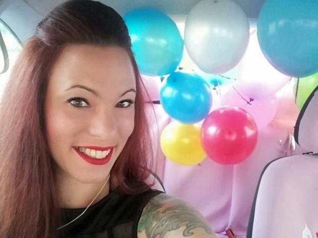 SexyAnnabell38-hot with red lipstick, smiling, tattoo on right arm, black top, brown hair, and colorful balloons in car, selfie.