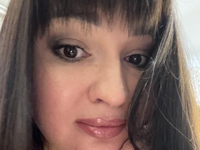 AlinaMilf's face with brown eyes, straight brown bangs, and glossy pink lips. Her nose is small, and her skin is light. Her eyelashes are dark and slightly wavy.