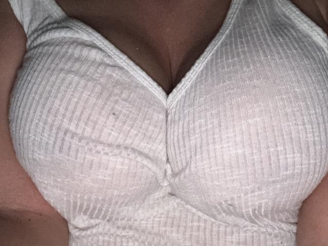 SeleneBright's big, white, ribbed, button-up, caged tits are visible in the shot, showing a tight, slightly wavy fabric that accentuates her ample cleavage.