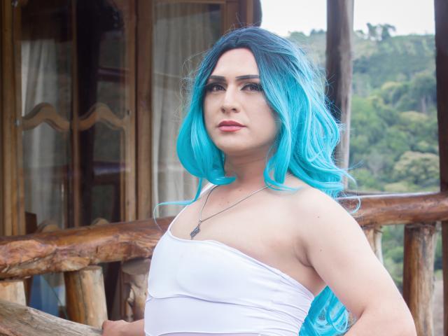 IrisDurand with bright blue hair, white strapless top, showing her tits, standing with hands on wooden railing, looking serious, wearing a necklace with a small pendant.