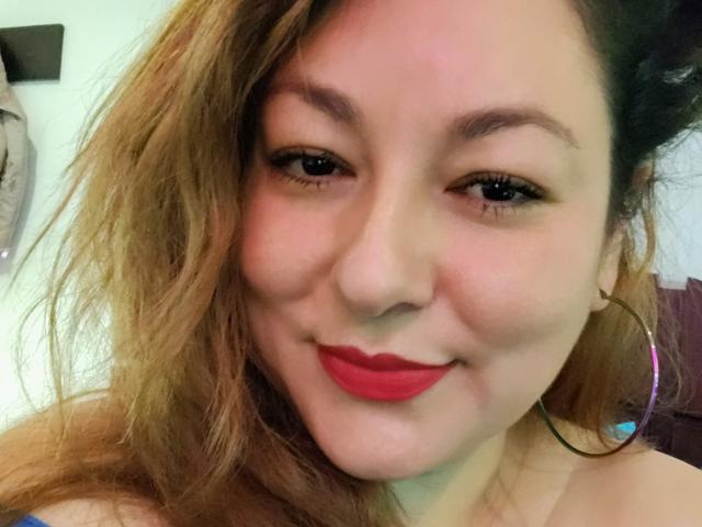SakotoDika hat ein süßes Gesicht mit hellbrauner Haut, rotem Lippenstift und kleinen Reifenohrringen. Sie hat welliges, blondes Haar und ein leichtes Lächeln. Ihre Brüste sind nicht sichtbar..
