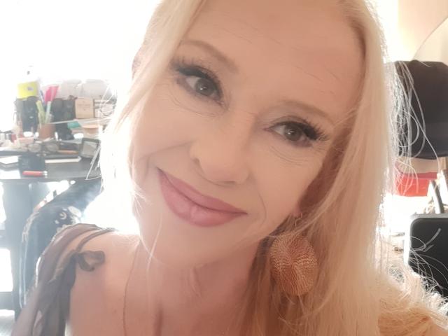 IssahneMay has blonde hair, long eyelashes, pink lipstick, and a cute smile. She's wearing a black strap and brown ear cuffs. Her tits are small, and she's sexy.