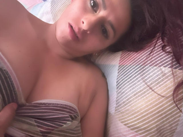 DylaraCollins has red hair, lying on a striped pillow, partially covering her tits with a striped shirt, looking up with a slightly open mouth, in a soft-lit photo.