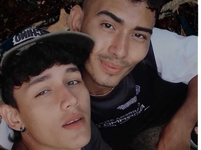 Two Alenders with curly black hair and light brown skin, one in a cap, both smiling, one with a slight beard, wearing dark shirts, looking at the camera.