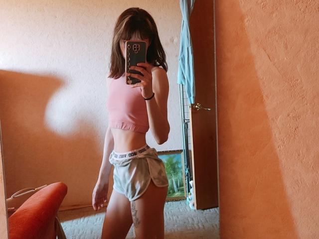 Barbariana with medium brown hair, pink sports bra, and gray "I JUST WANT PANTS" shorts, taking a mirror selfie, showing her slim, toned ass and flat tits.