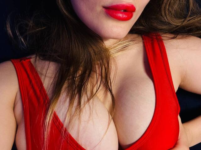 TenderAmberr's red dress, showcasing her big tits and red lips, with brown hair partially covering her face. Her hand rests near her chest.