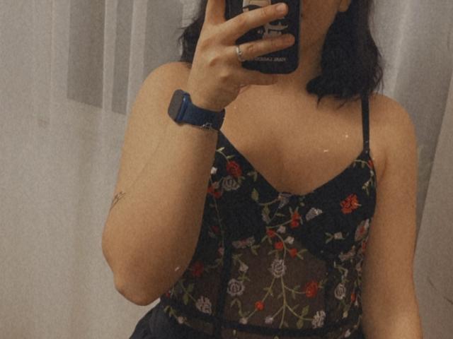 Denise69s taking a mirror selfie wearing a black, sheer, floral-embroidered top with red and white flowers, showing her tits and wearing a blue smartwatch.