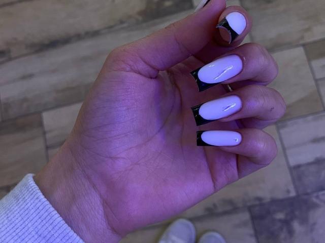 La mano de Kripkoa, con uñas blancas brillantes y puntas negras, y un anillo de plata en el dedo índice, lleva una manga blanca, mostrando sus uñas en una foto..