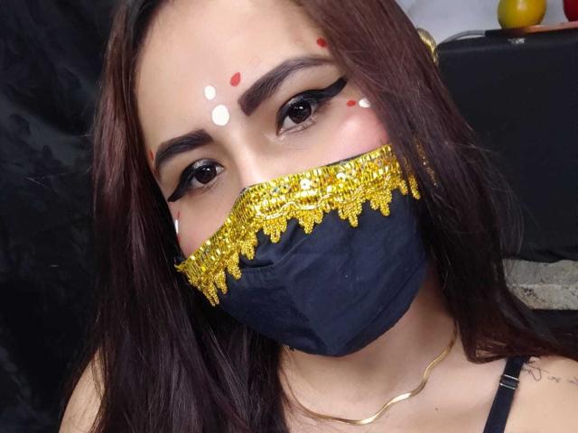 Dalia Dubey, met donkerbruin haar, een zwart masker en goudglitters op haar gezicht, draagt opvallende zwarte eyeliner en rode stipjes, met een gouden ketting, en kijkt naar de camera..