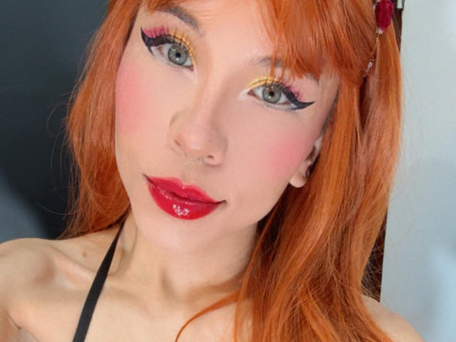 SofiBrandford with orange hair, pink eyeshadow, black eyeliner, red lipstick, and a black halter top, showing a cute, sexy face. Her tits are not visible.
