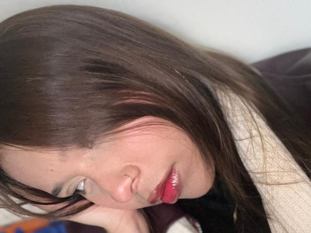 HeraJuno with shiny red lips, slightly parted, brown hair, pale skin, and a soft, sleepy expression, leaning forward with her face angled downward.
