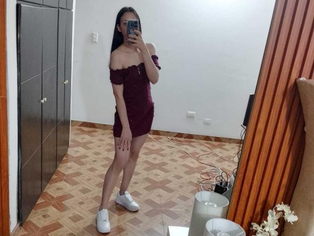 KarlaaGil, wearing an off-shoulder maroon dress and white sneakers, stands in a mirror selfie with long black hair, holding a phone, showing her ass and small tits.