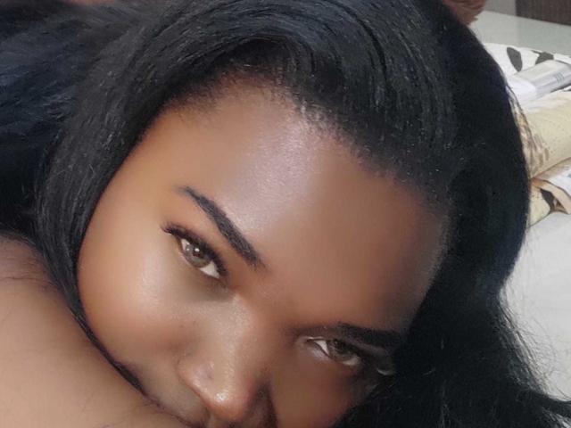 Janniz's face with dark brown skin, black hair, and brown eyes, looking up with a slight smile, her smooth skin and thick eyebrows clearly visible.