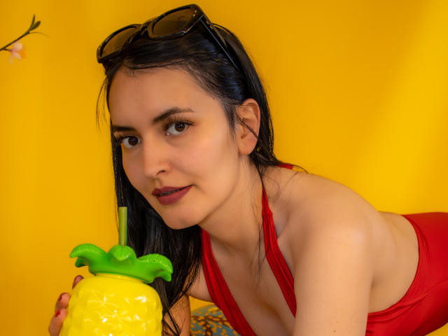 AriaBonnet with wet black hair, red bikini top, holding yellow pineapple drink, sunglasses on head, yellow background, smiling, fair skin, small tits, brown eyes, dark red lipstick.