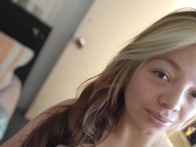 ScarlettAmelia with light brown, wavy hair, smiling slightly, has fair skin and brown eyes, wearing nothing visible, in a soft lit room, upper body focused.