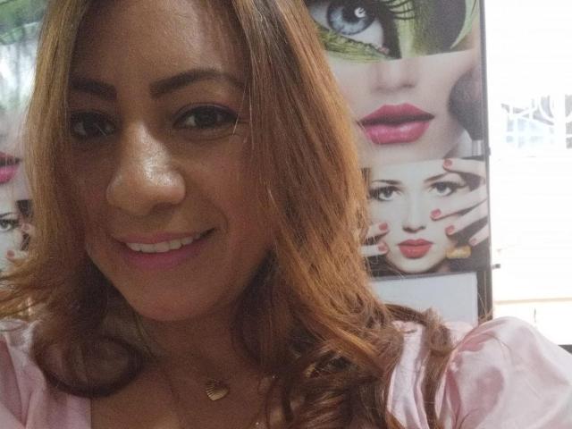 Britney69 has medium brown skin, long wavy brown hair, and a smile showing white teeth. She's wearing a pink shirt, and a gold necklace with a small heart.