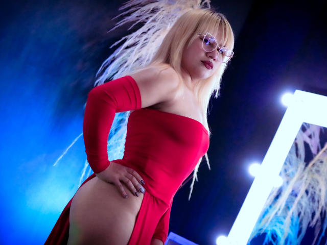 LilithCastelli with blonde hair, glasses, red strapless dress, and long sleeves, showing her ass with a hand on it, in a blue-lit, mirror-filled room.