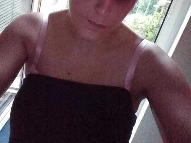 Sexybienchen93-hot with light pink straps on a black top, showing a small mole on their chest, and a slight, cute smile. Upper body, dim lighting, casual.
