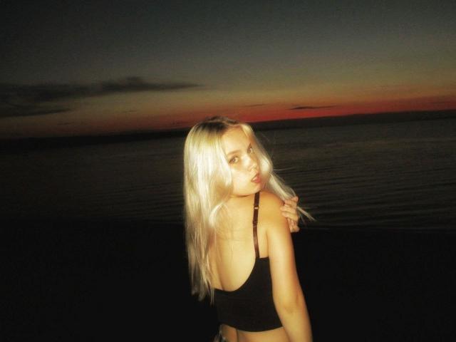 KarosLove with long blonde hair, black sports bra, looking over shoulder, dark water, sunset, soft lighting, slightly disheveled, hand on shoulder, subtle smile, sexy, attractive.