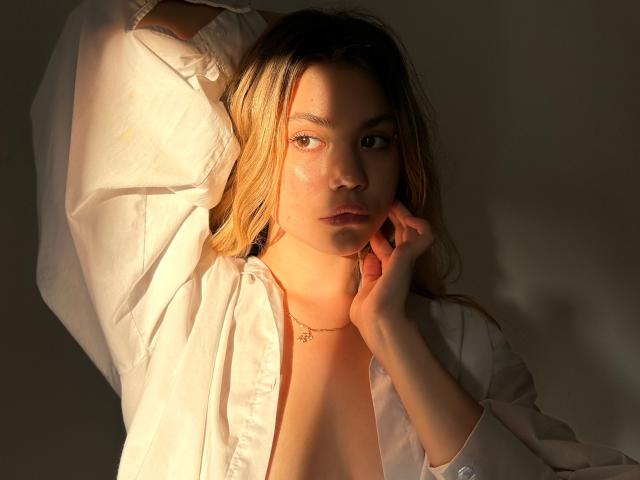 SweetLime with blonde hair, wearing an open white shirt, exposing her tits, sunlight on her face, hand touching her cheek, looking to the side, gold necklace.