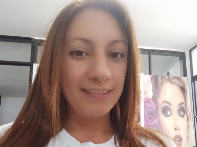 Britney69 has medium brown hair, a light skin tone, and a cute smile. She's wearing a white top, and there's a portrait of a woman with purple roses behind her.