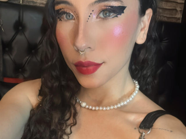 SofiBrandford with curly black hair, red lipstick, black eyeliner, pearl necklace, nose ring, and blush, showing tits and a cute face.