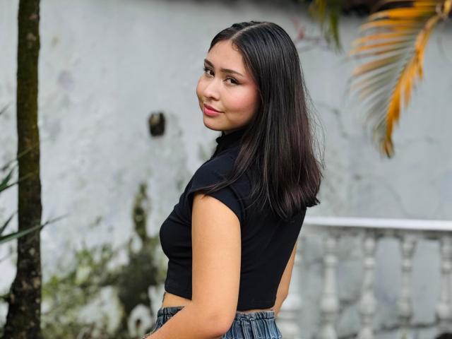 BellaMiaI with shoulder-length black hair, wearing a sleeveless black top and blue jeans, looking over her shoulder with a subtle smile, showing her small, cute ass.