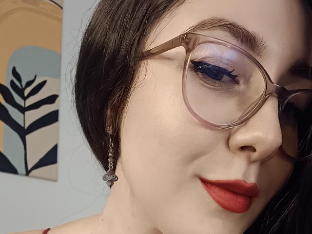 MabyLegrand's face, pale skin, red lipstick, blue eyeshadow, glasses, black hair, small hoop earrings, slight smile, soft light. Boobs not visible. Ass not visible. Tits not visible.