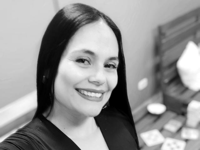 Black-and-white selfie of CharlotteCrofort with long dark hair, smiling, nose ring, and wearing a black top, showing her teeth and earrings. Her tits are not visible.