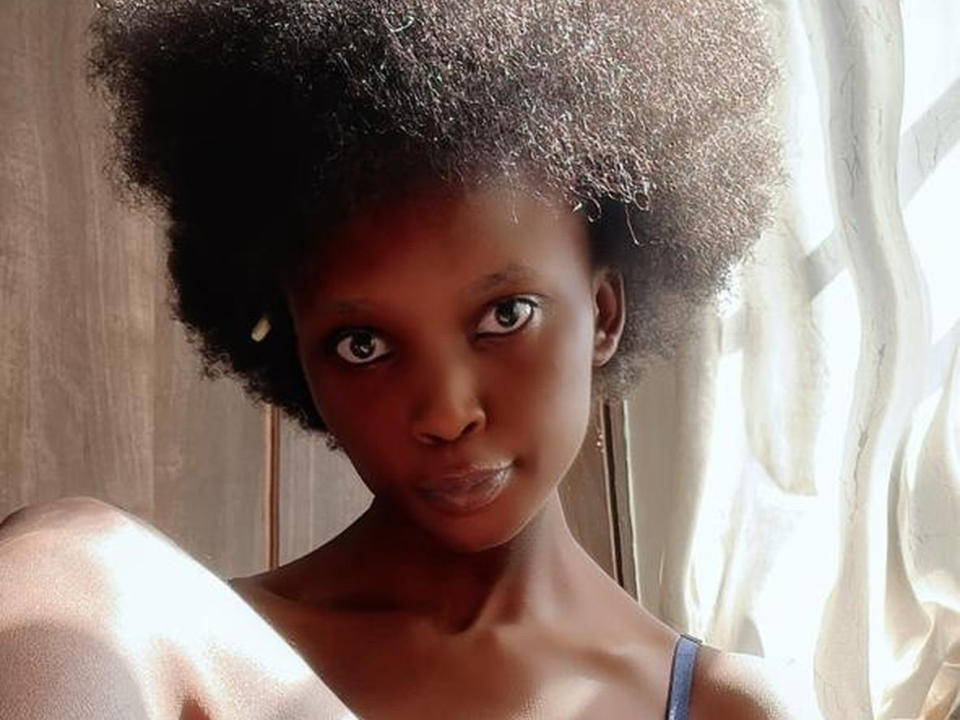 HippieShanice has dark brown skin, a big afro, and is wearing a blue tank top, with sunlight highlighting her face and shoulder. She has small, shiny earrings.